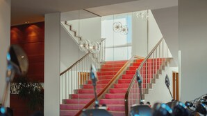 Un interior moderno con una escalera, barandilla de vidrio y una lámpara en el techo.
