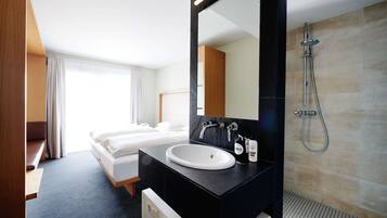A hotel room with a bed, a bathroom with a sink, mirror, and shower.