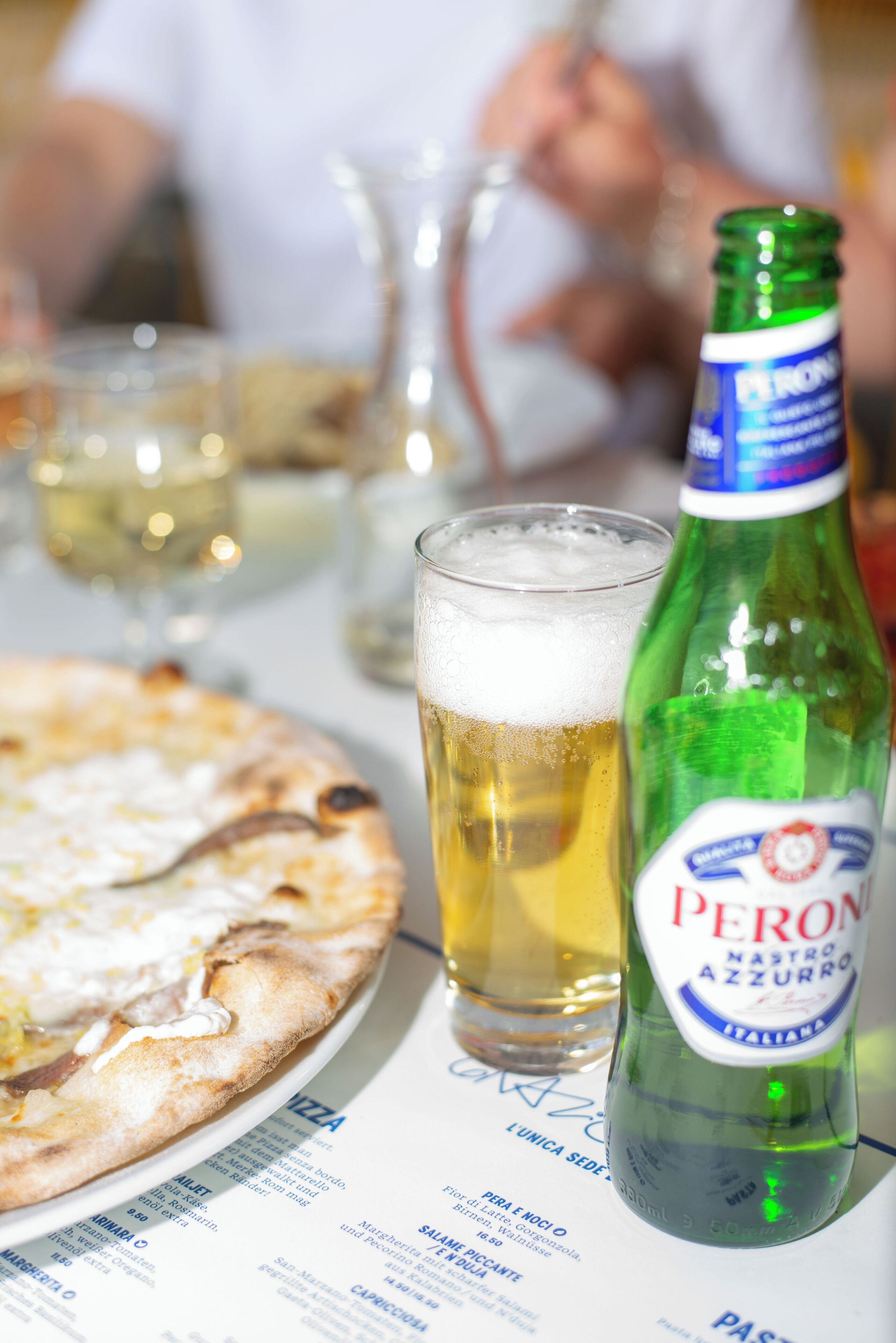 Una pizza, una cerveza y una botella de cerveza Peroni sobre una mesa.