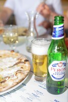 Una pizza, una cerveza y una botella de cerveza Peroni sobre una mesa.