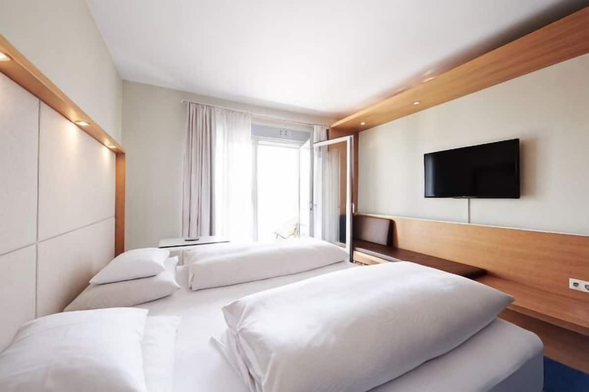 A hotel room with a bed, a TV, and a window with curtains.