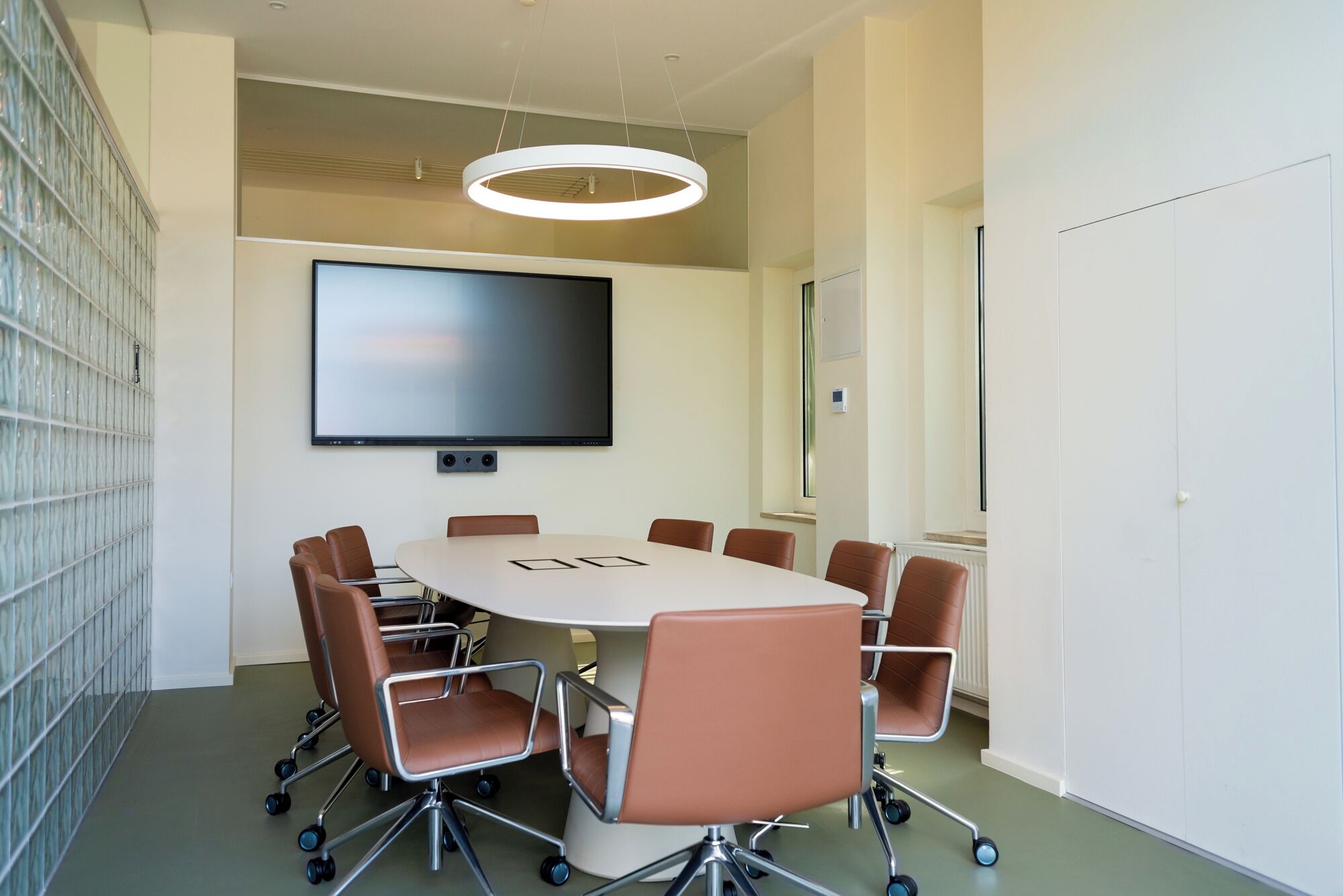 A conference room with a large flat-screen TV, a round table, and six chairs.