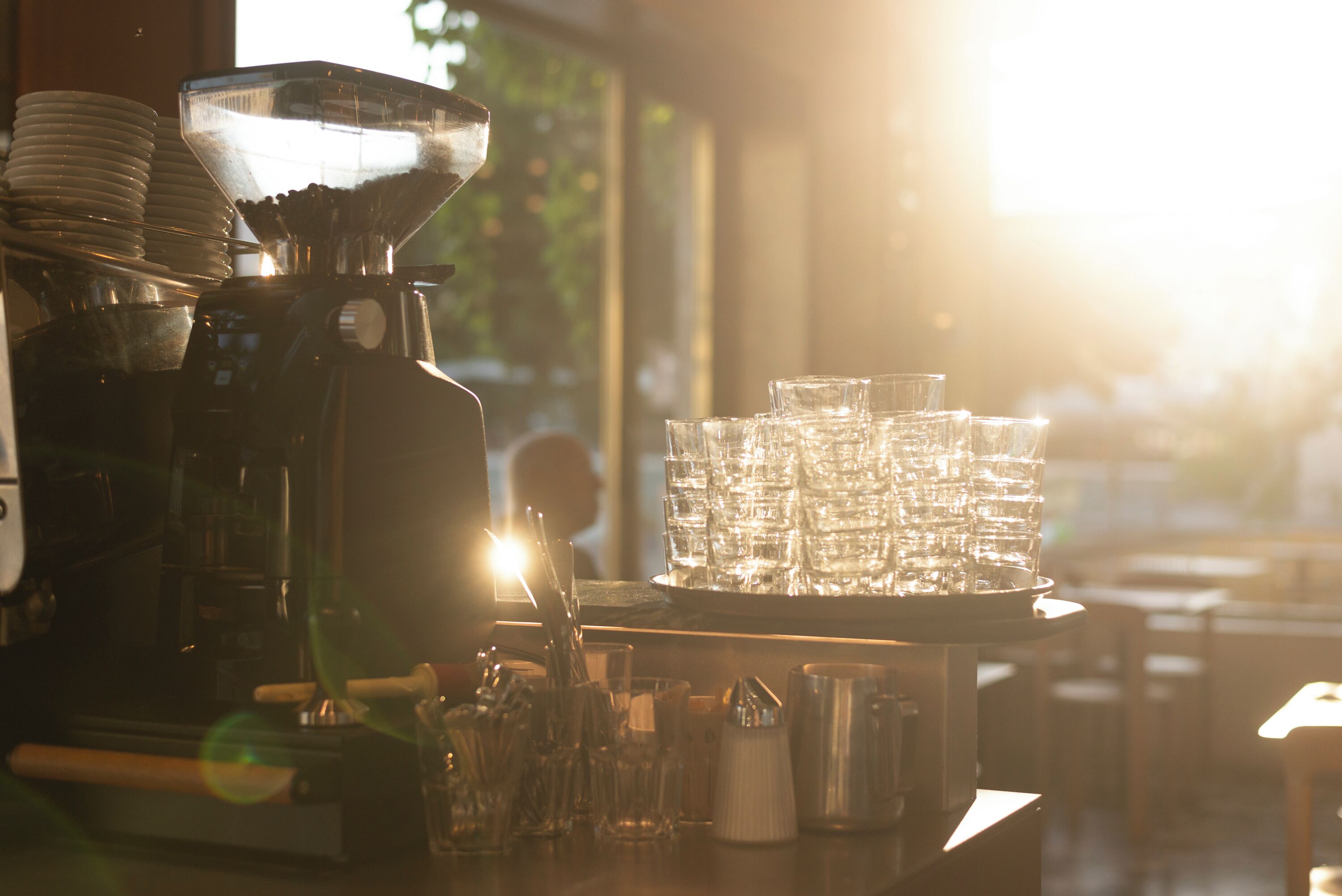 A coffee machine, stacked glasses, and a tray of cups in a cafe setting.