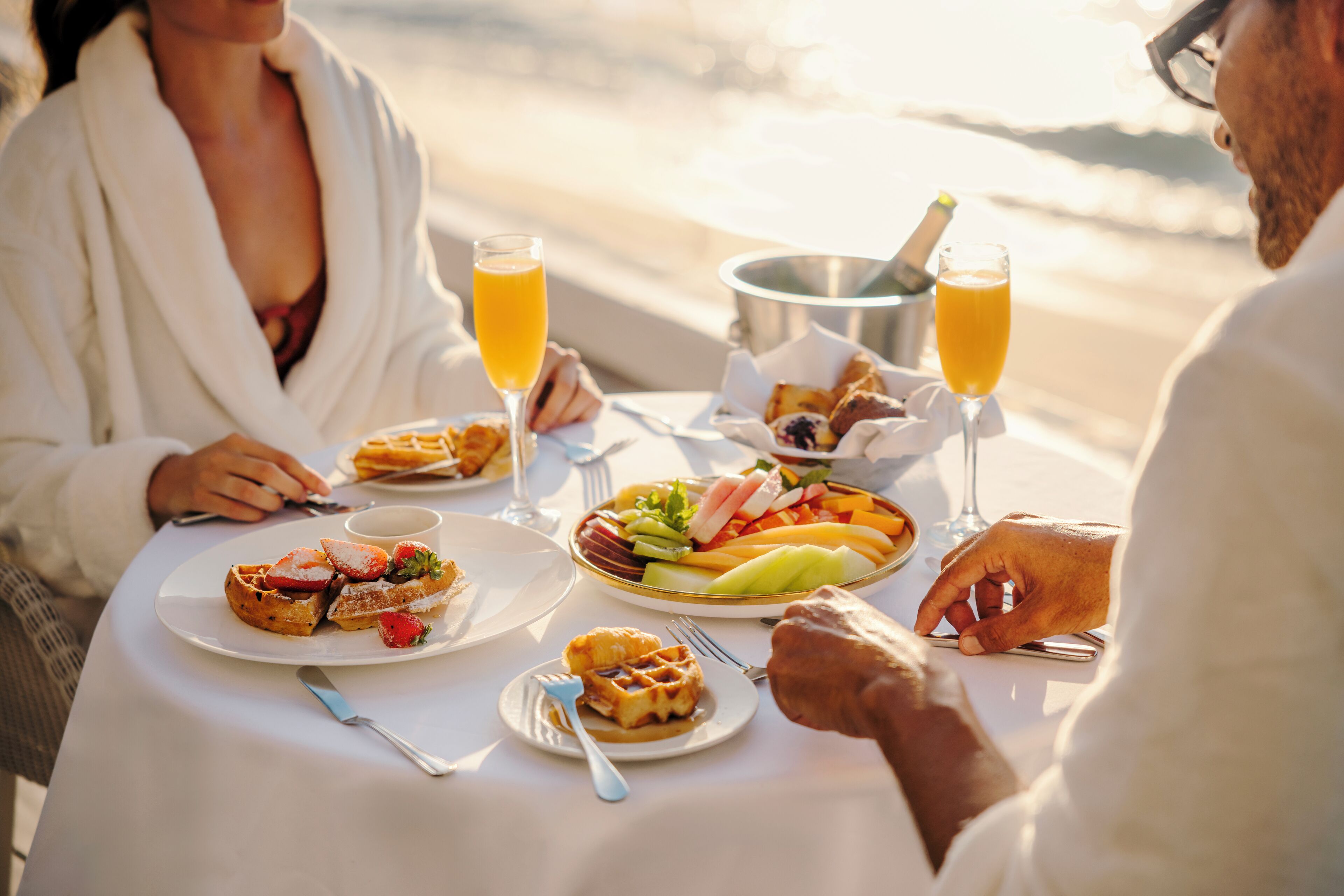 Une table à manger dressée avec des aliments et des boissons pour le petit-déjeuner, donnant sur une plage.