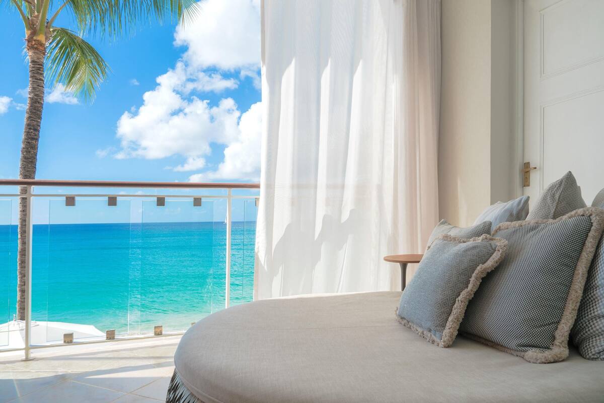 Ein Schlafzimmer mit Meerblick, ein Balkon mit einer Palme und ein Bett mit gemusterten Kissen.