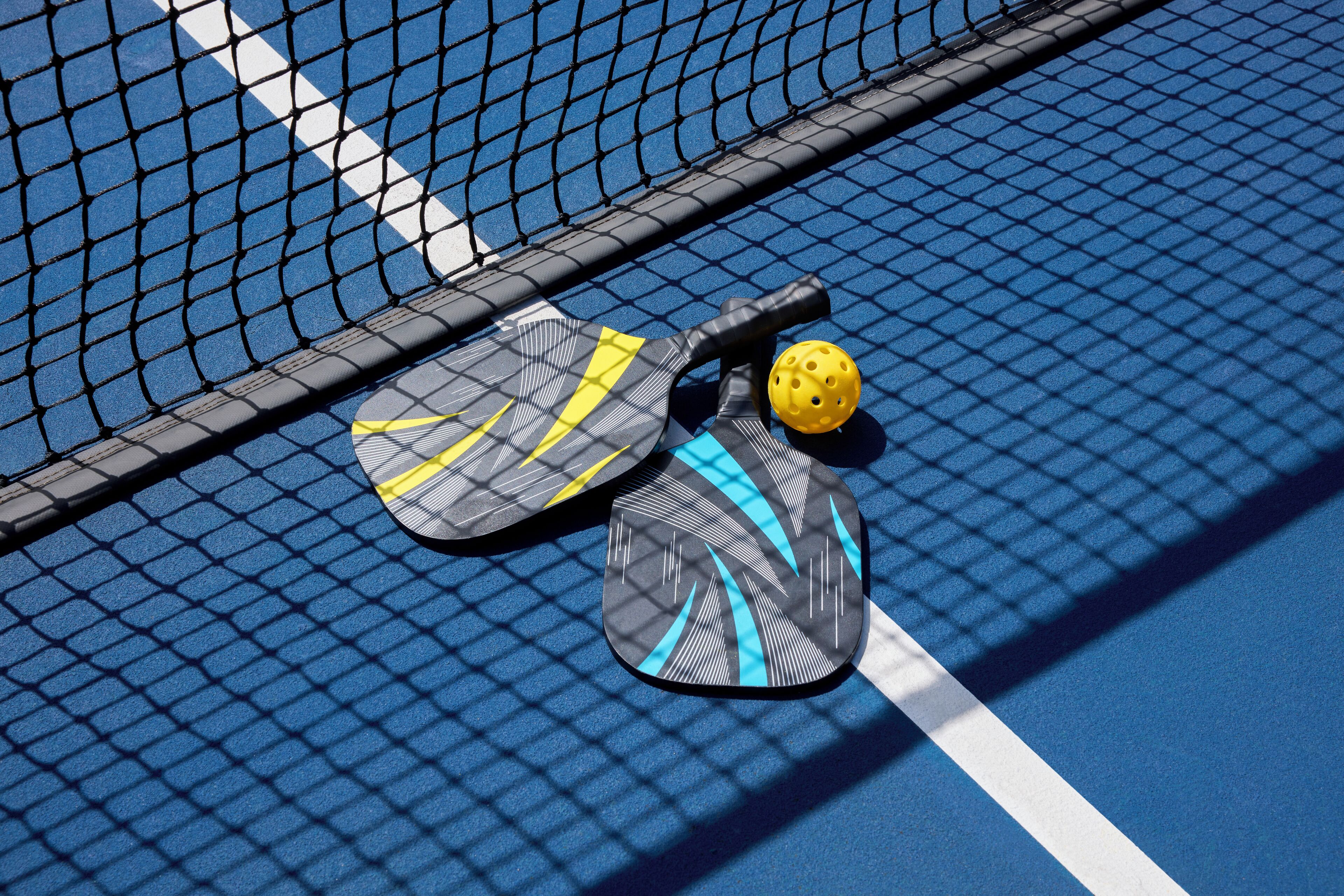 En tennisbane med net, to tennisraketter og en gul tennisbold.