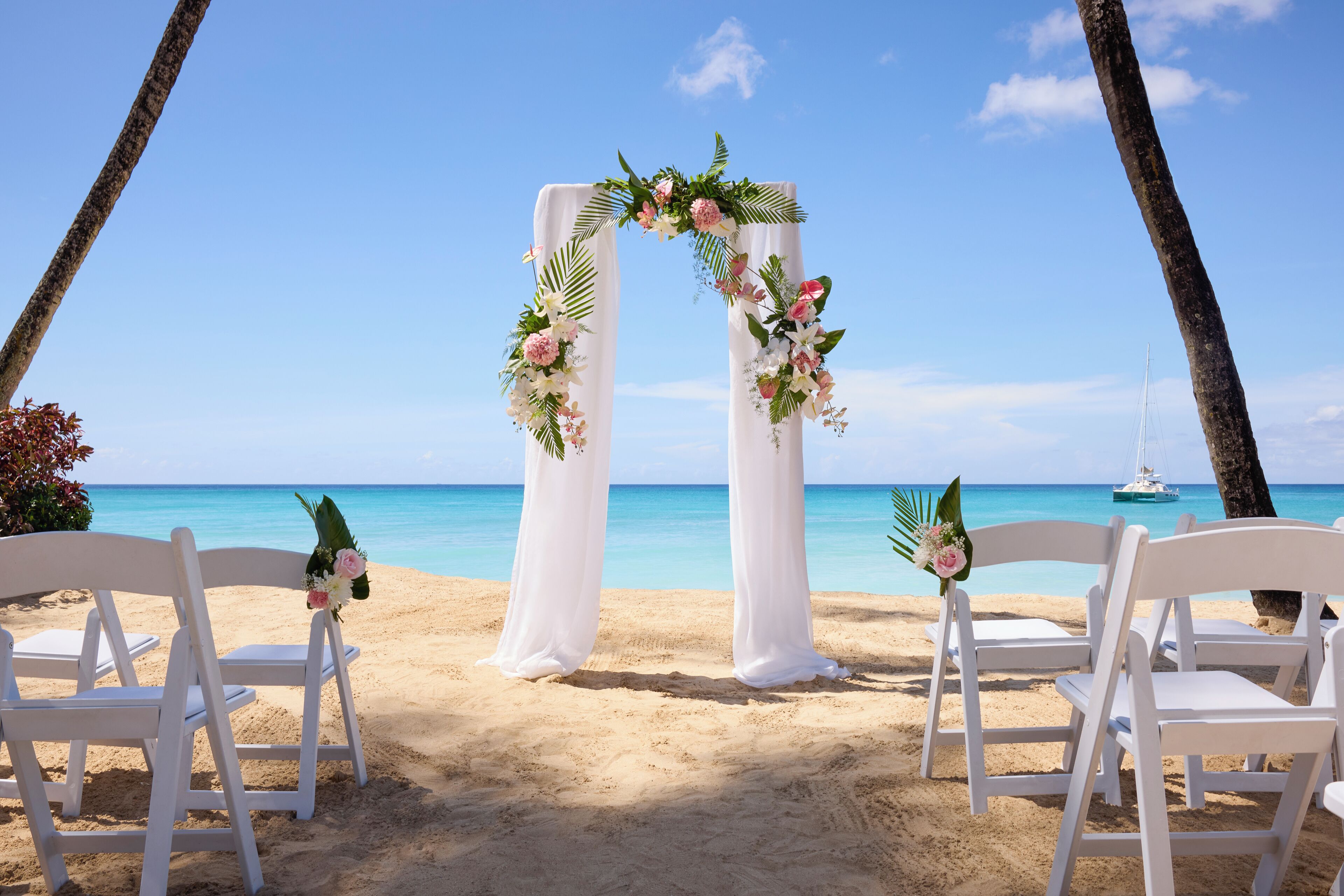 A beach wedding setup with white chairs and a floral arch.