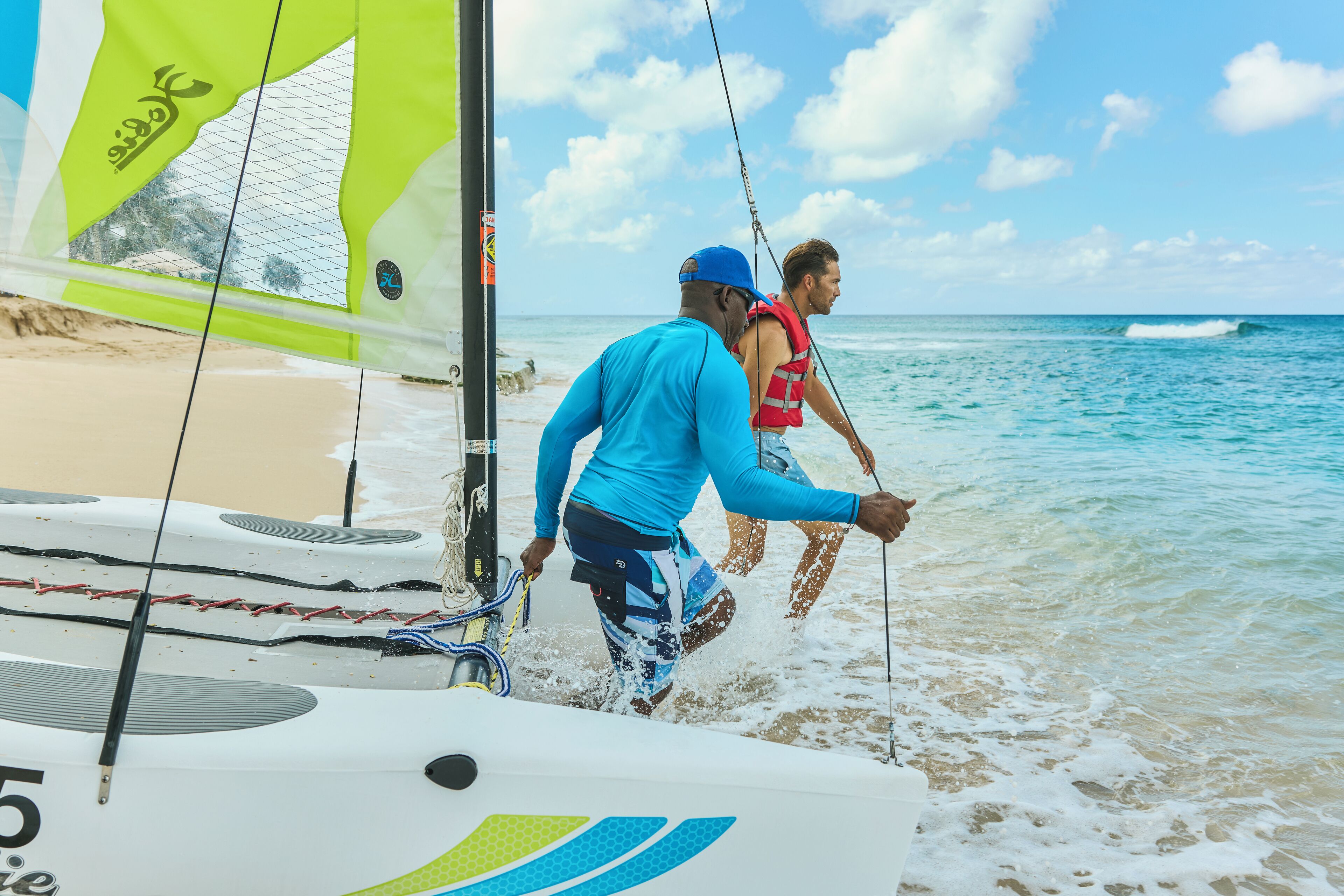 A sailboat with a person in a blue shirt and a life jacket on the beach.