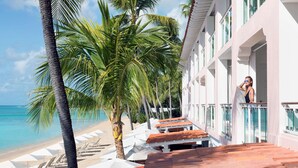 Un hotel frente a la playa con piscina, palmeras y vista al océano.