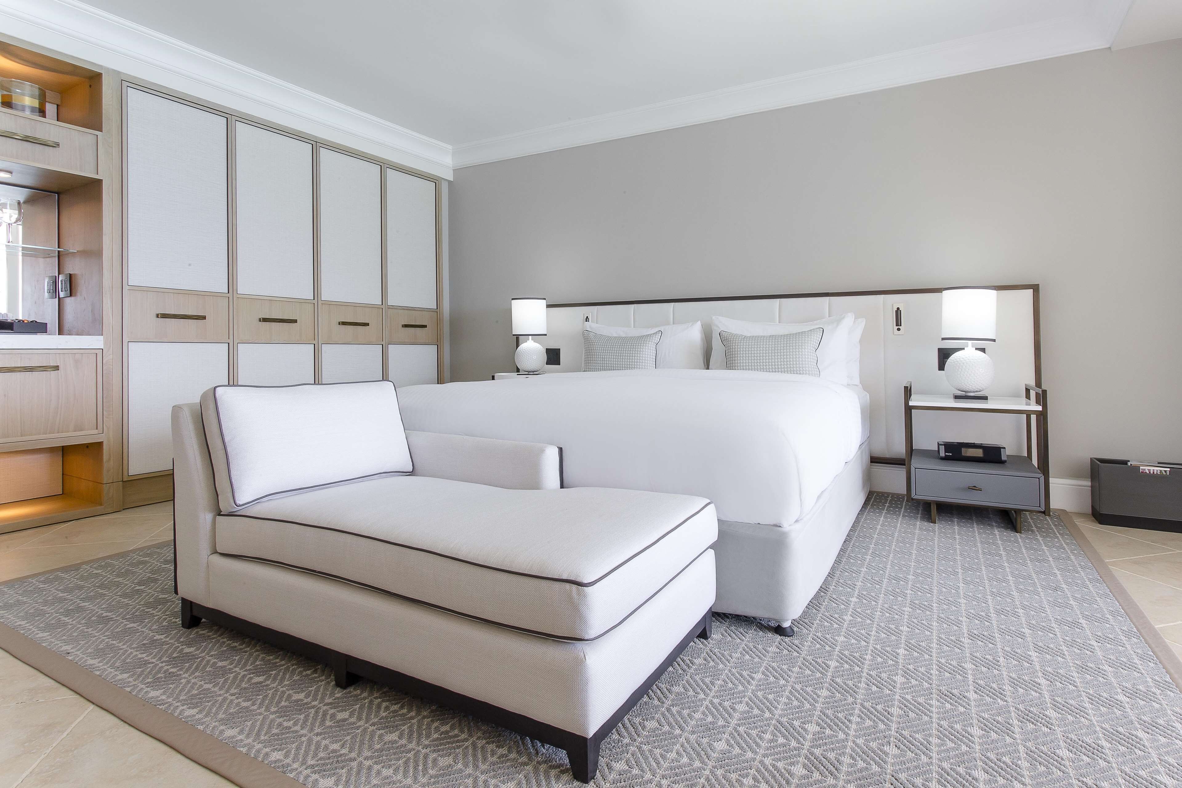 A hotel room with a large bed, a sofa, a wardrobe, and a nightstand with lamps.