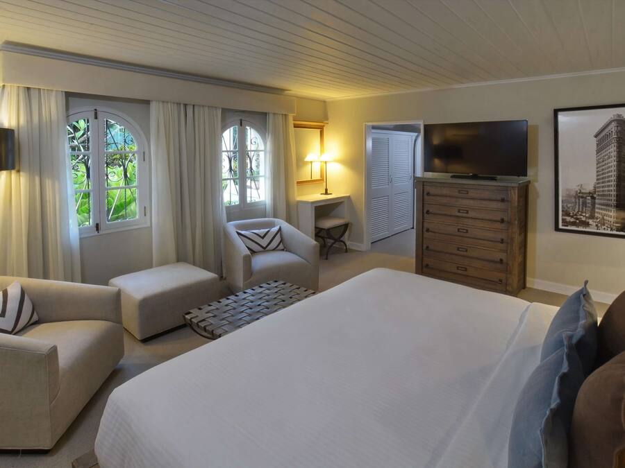 A hotel room with a large bed, a sofa, a chair, a TV, and a painting of a building.