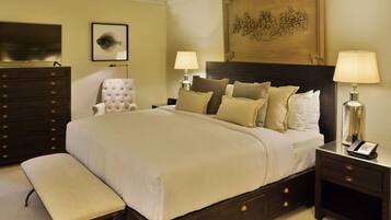 A neatly arranged bedroom with a large bed, a bedside table with a lamp, a chair, a dresser, and a television on the wall.