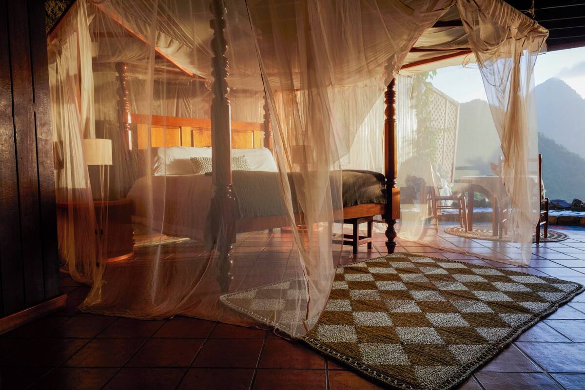 A four-poster canopy bed with a checkered rug, wooden furniture, and a view of mountains.