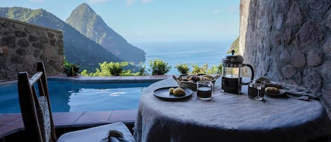 A table set with breakfast items overlooking a pool and mountains.