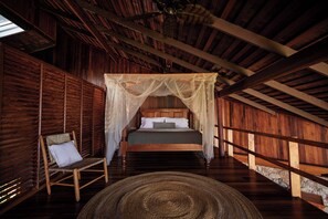 A wooden room with a bed, a chair, and a large woven rug.