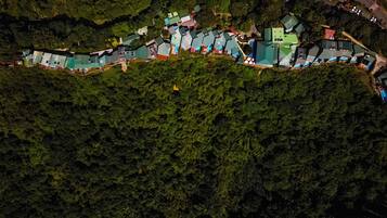 An aerial view of a residential area with houses arranged in a linear fashion along a road, surrounded by dense forest.