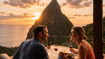 A couple dining at a table with a view of a mountain and the ocean during sunset.