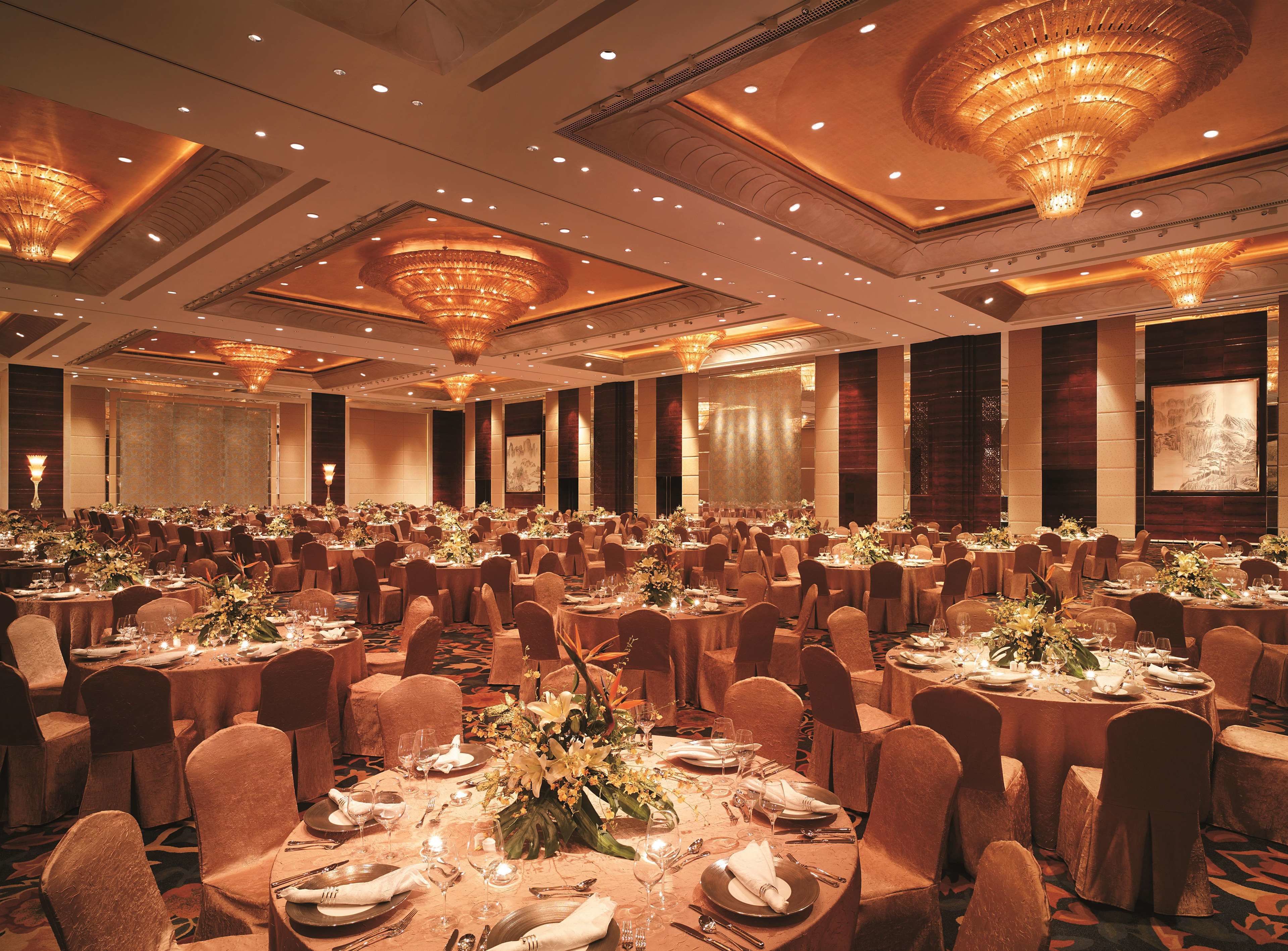 A banquet hall with round tables, chairs, and chandeliers.
