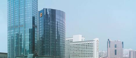 A high-rise building with a glass facade, surrounded by other buildings and greenery.