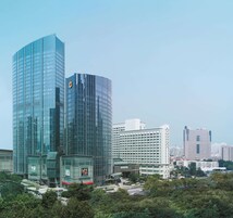 Un edificio de gran altura con fachada de vidrio, rodeado de otros edificios y vegetación.