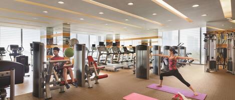 Une salle de sport équipée de matériel d'exercice, de tapis de yoga et où une personne fait des étirements.