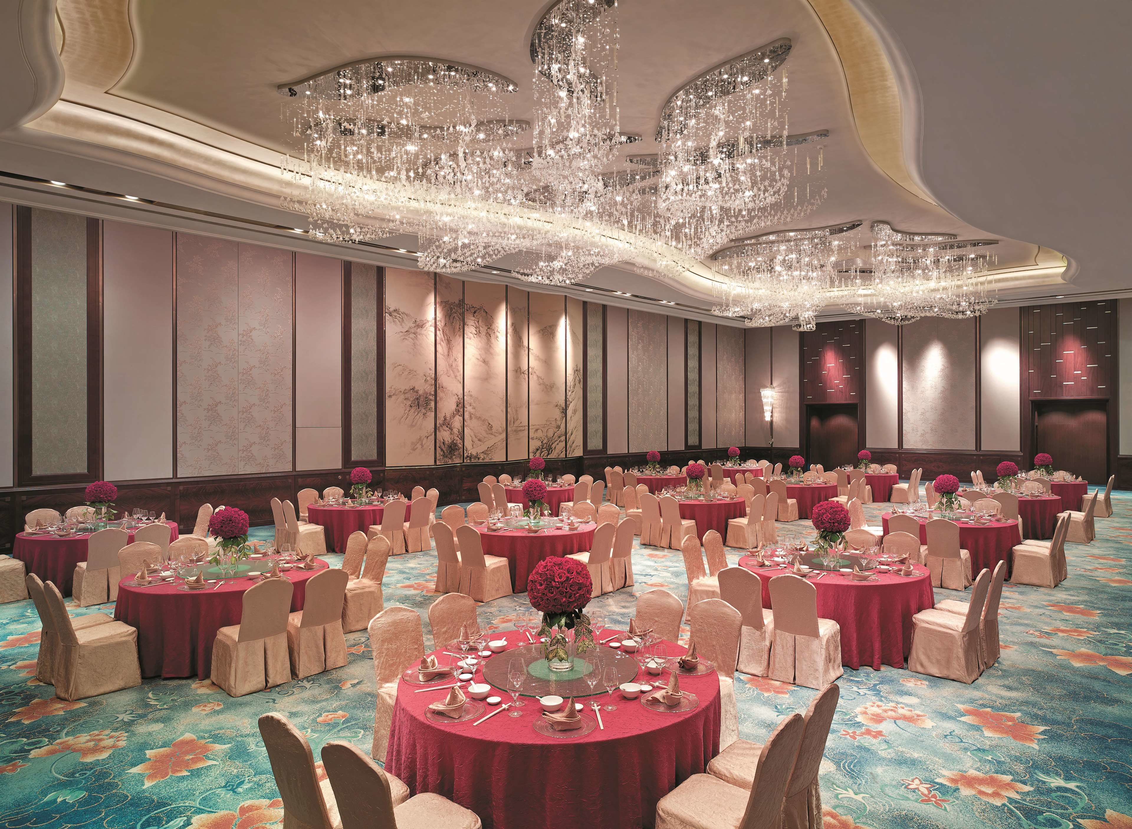 Un salón de banquetes con mesas redondas, sillas y una gran lámpara de araña.