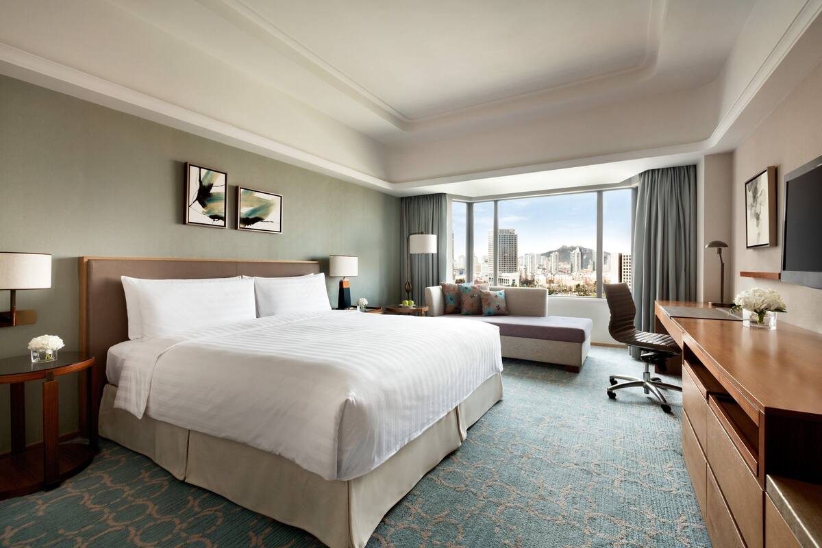 Ein Hotelzimmer mit einem großen Bett, einem Schreibtisch, einer Couch und Blick auf die Stadt.