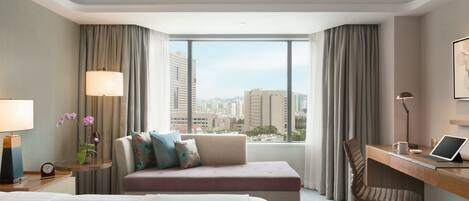 A hotel room with a bed, a desk, a chair, a view of the city, and a window with curtains.