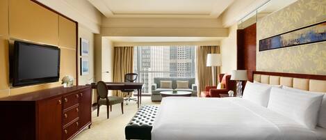 Ein Hotelzimmer mit einem großen Bett, einem Schreibtisch mit Stuhl, einem Fernseher und Blick auf die Stadt.