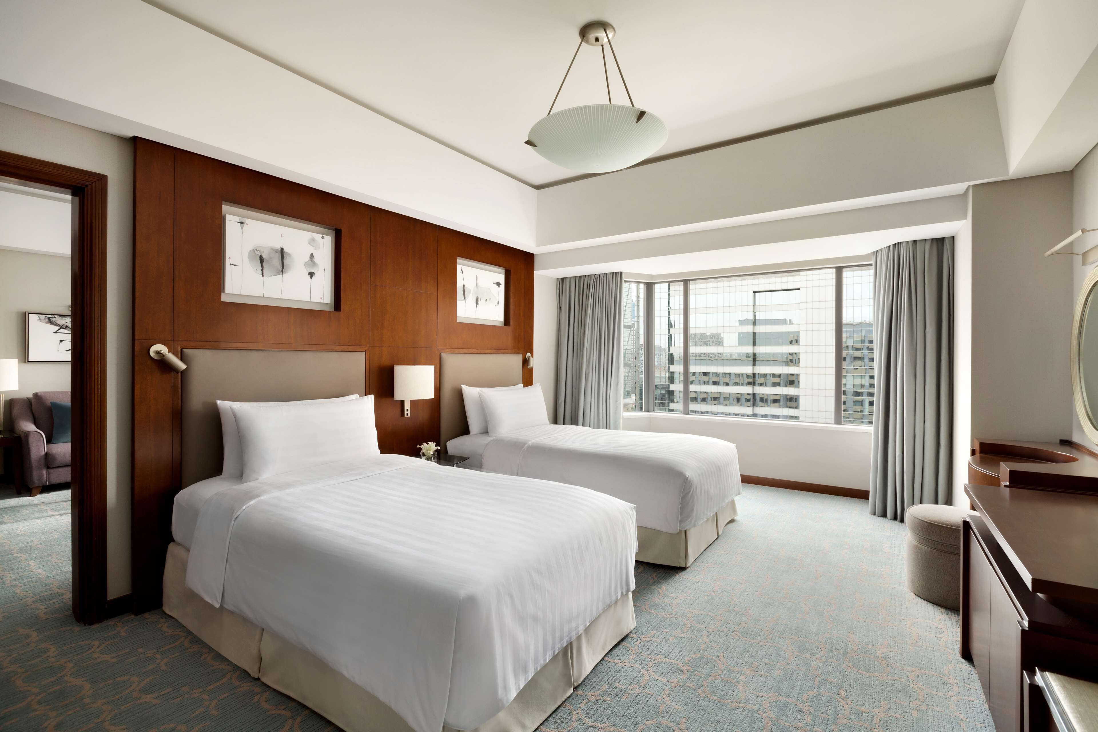 Una habitación de hotel con dos camas, un ventanal con cortinas, un escritorio y un espejo.