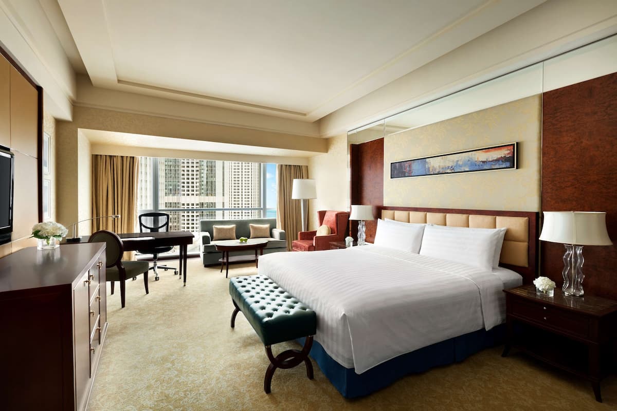 Ein Hotelzimmer mit einem großen Bett, einem Schreibtisch, einem Sessel, einer Couch und einem Fenster mit Blick auf die Stadt.