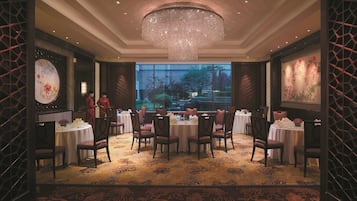 A dining area with round tables, chairs, and a large chandelier.