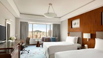 A hotel room with a large bed, a desk, a chair, a sofa, and a view of a cityscape.