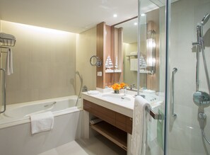 A modern bathroom with a bathtub, two sinks, a glass-enclosed shower, and a mirror with a ship decoration. - Shangri-La Qingdao (Qingdao)