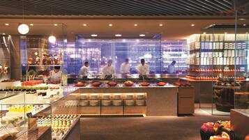 A modern kitchen with chefs preparing food, a display of fruits and vegetables, and a variety of dishes on the counter.