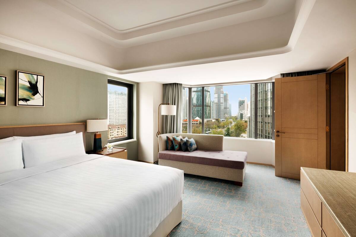 Ein Hotelzimmer mit einem großen Bett, einem Sofa, einem Schreibtisch und Blick auf die Stadt.