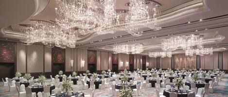 A banquet hall with round tables, white chairs, and floral centerpieces.