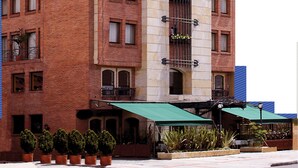 Un hotel con una torre dell'orologio, diversi balconi con piante e un tendone verde sull'ingresso.