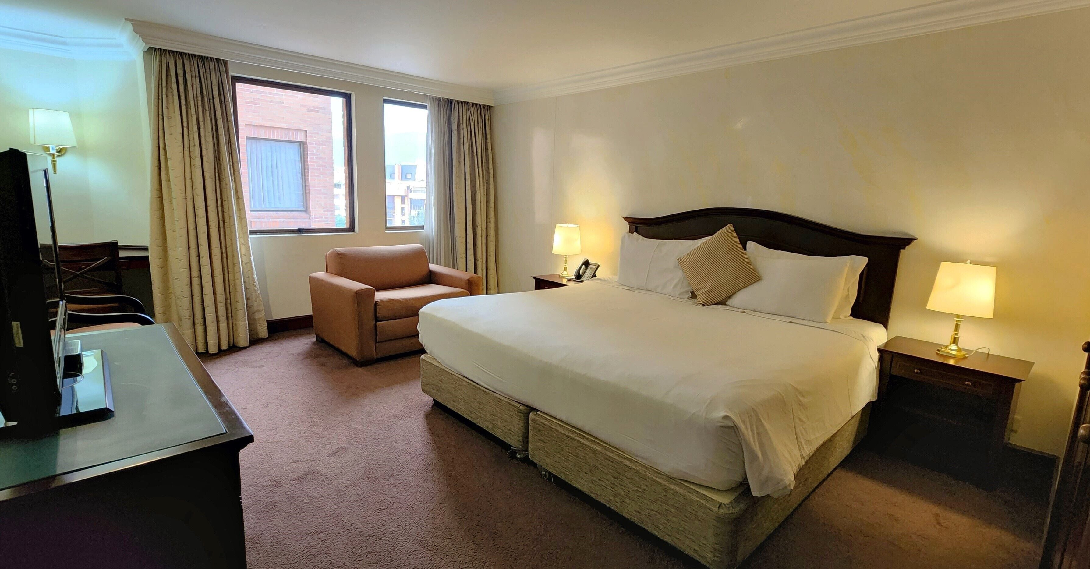 A hotel room with a large bed, a chair, a desk, and two bedside lamps.