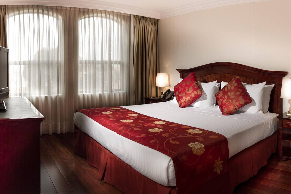 Ein Hotelzimmer mit einem großen Bett, einem Schreibtisch, einem Sessel, einem Fernseher und einer Lampe.