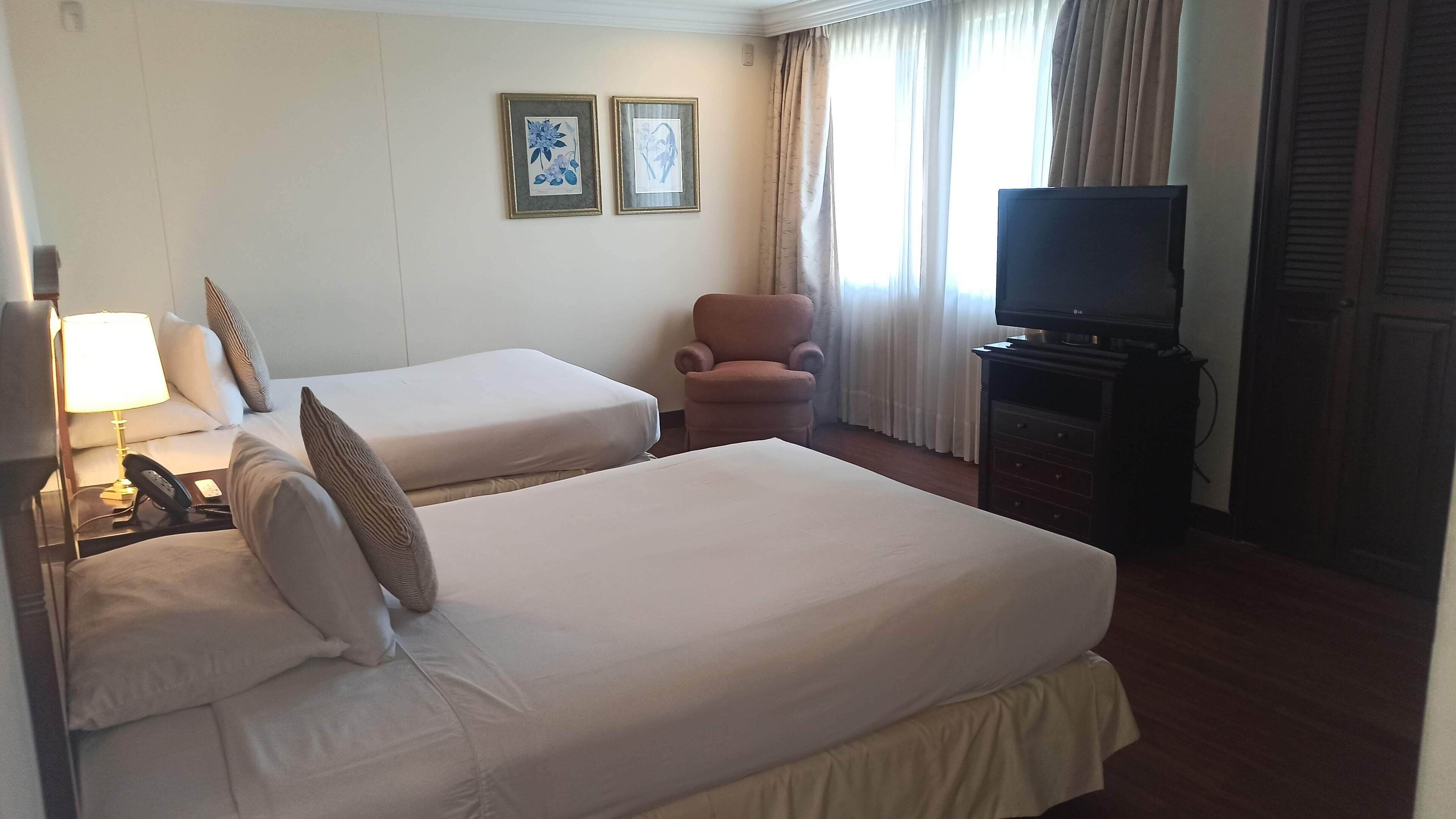 Habitación de hotel con dos camas, una silla, un televisor y una lámpara.