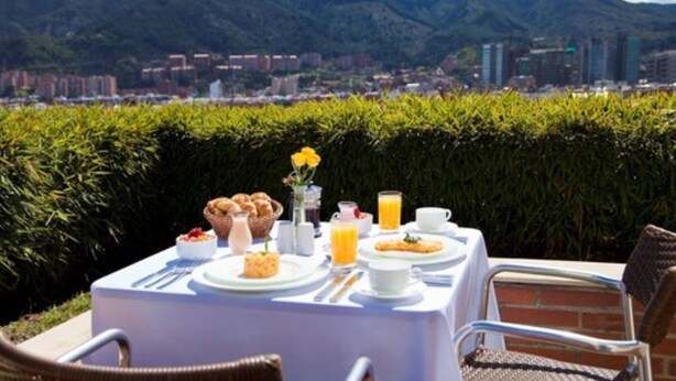 Tavolo apparecchiato all'aperto con prodotti per la colazione, con vista su una città e montagne.
