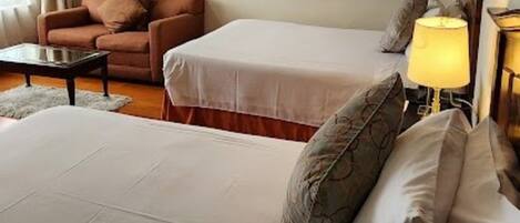 A hotel room with two beds, a sofa, a coffee table, and two framed pictures on the wall.