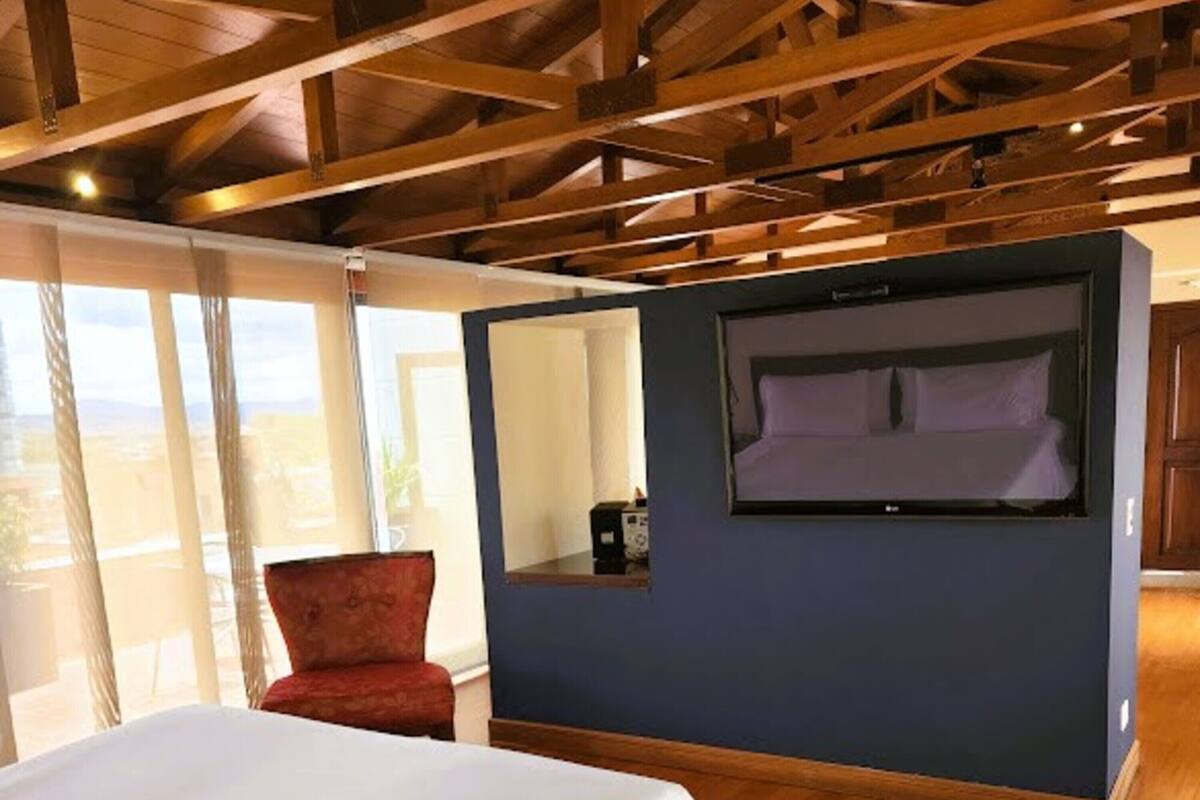 Ein Schlafzimmer mit einem großen Bett, einem roten Sessel, einem integrierten Fernseher und einem Balkon mit Blick.