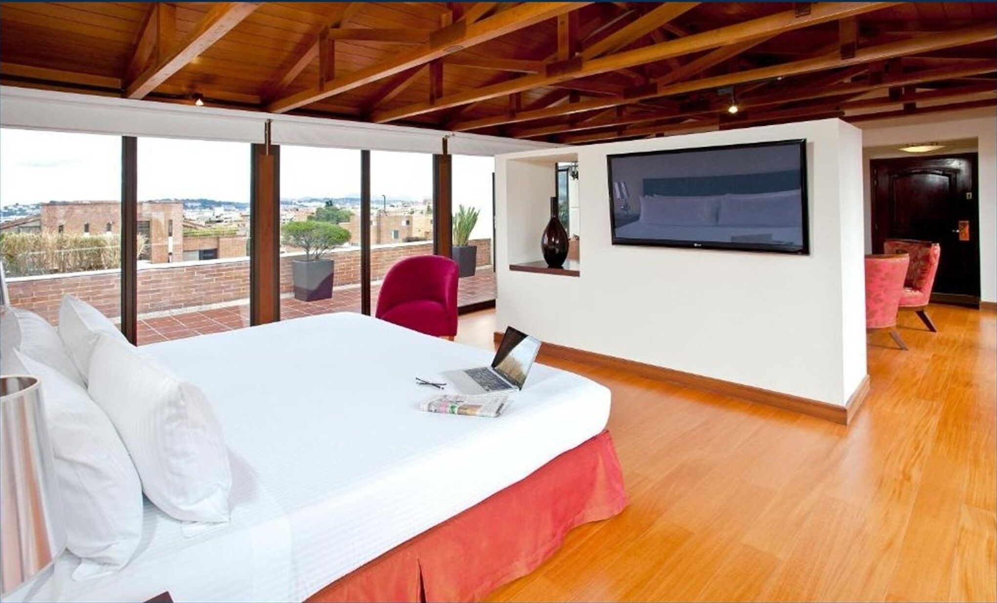 Une chambre avec un grand lit, un ordinateur portable, une télévision et une vue sur la ville.