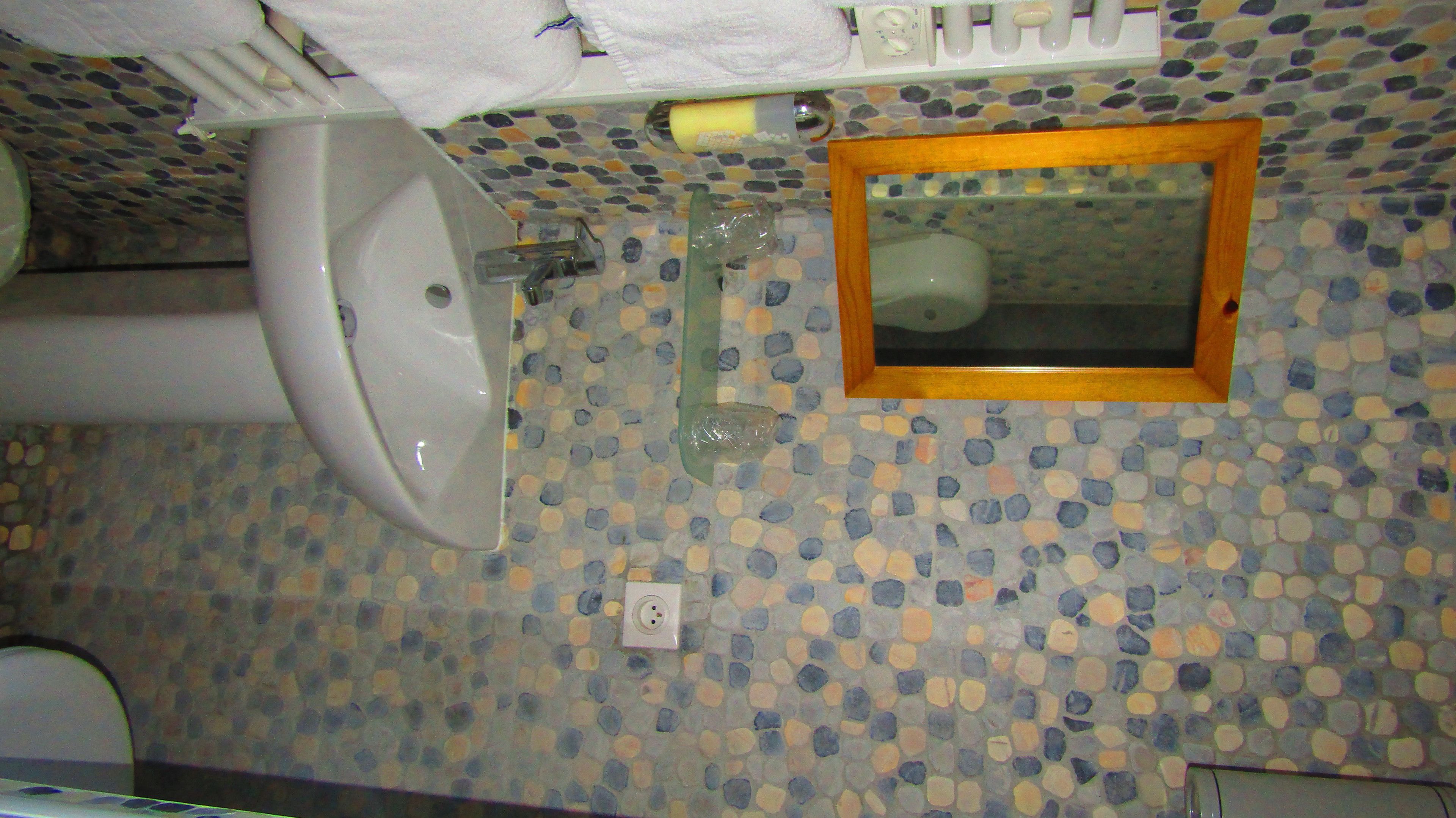 Un baño con suelo de mosaico, un lavabo blanco y un espejo con marco de madera.