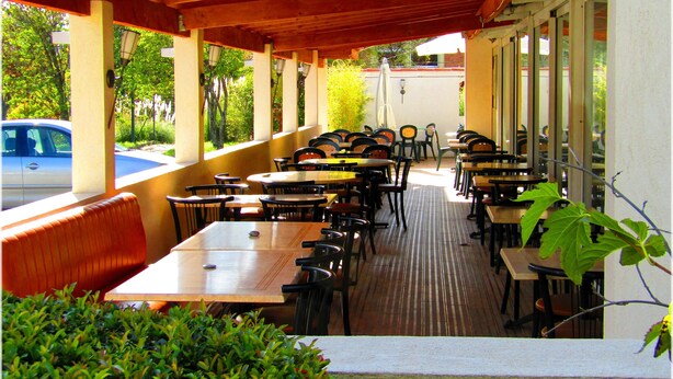 An outdoor patio with multiple tables and chairs, a wooden bench, and a view of a street with a parked car. - Aix Hotel (Aix-en-Provence)