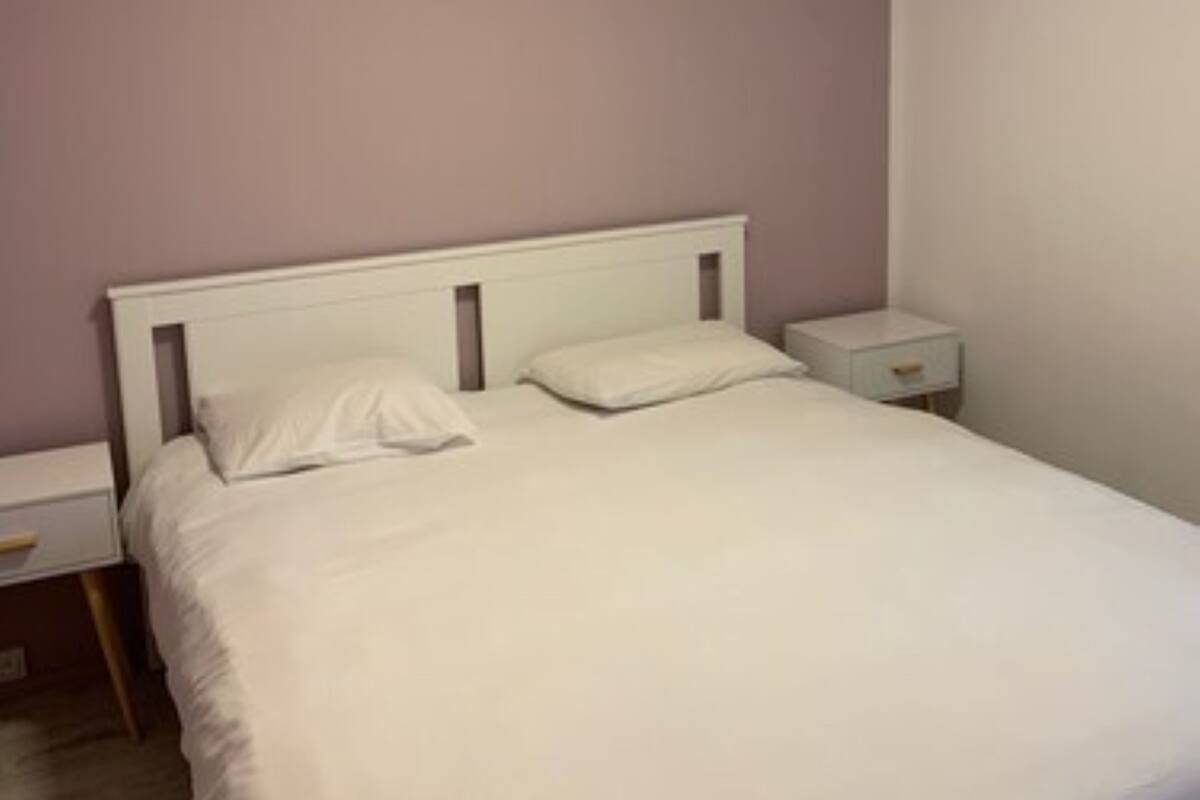 A bedroom with a single bed, white bedding, a nightstand, and a bedside table.