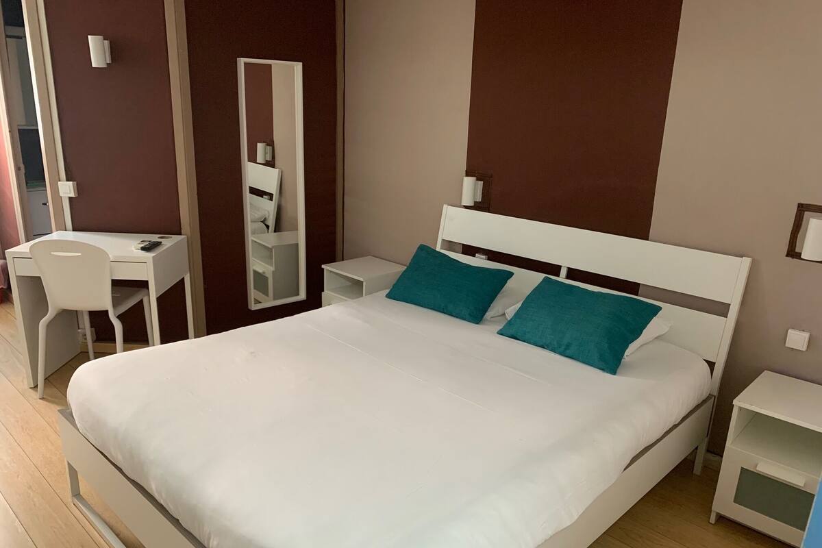 A neatly arranged bedroom with a large bed, a desk, and a chair.