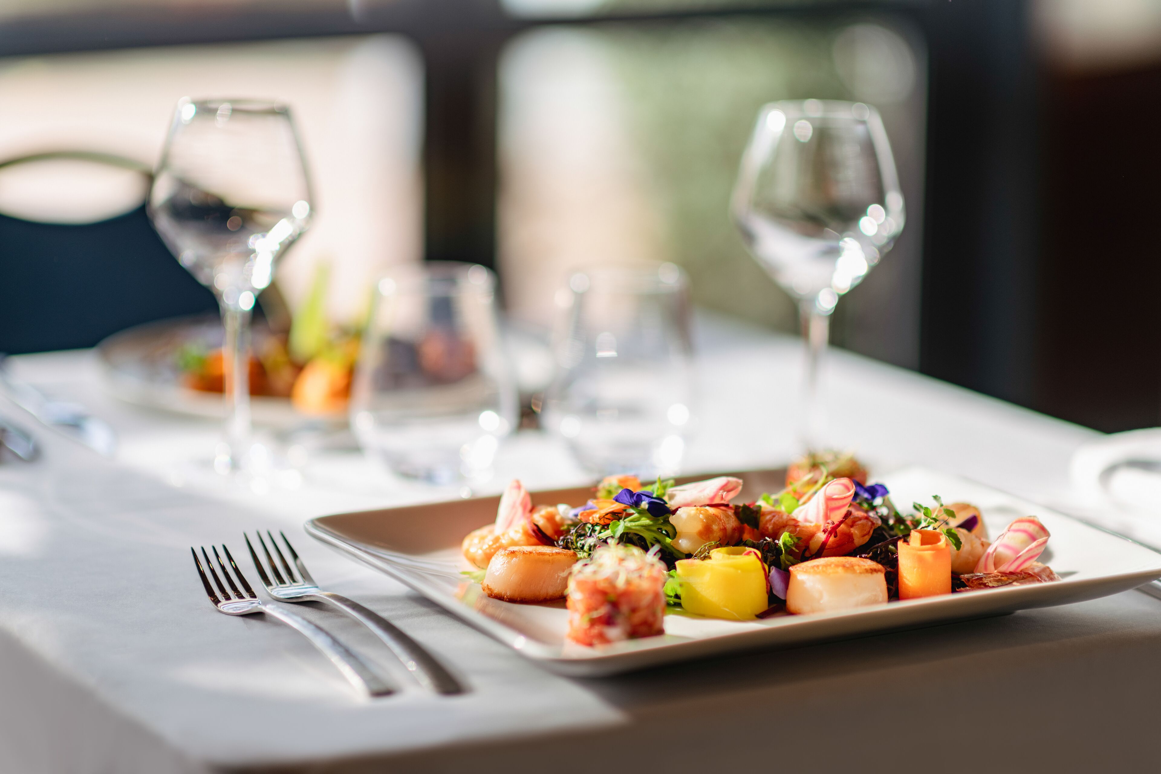 A dining table with a plate of food, cutlery, and wine glasses.
